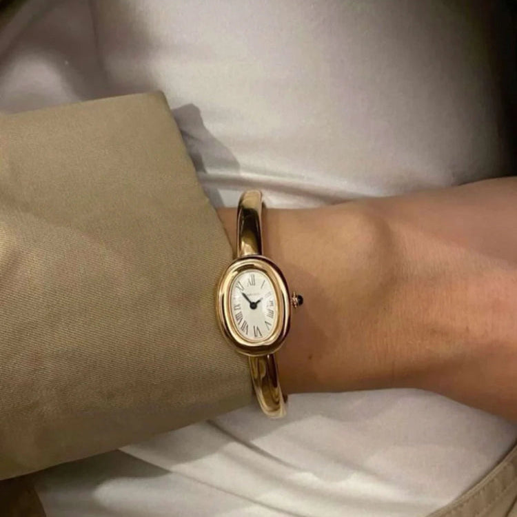 Gold wristwatch on a person's wrist with a neutral background